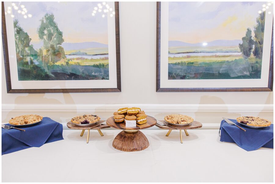 A dessert table at Pembroke Pines Country Club in Pembroke, NH, featuring pies and pumpkin whoopie pies, displayed under landscape paintings.