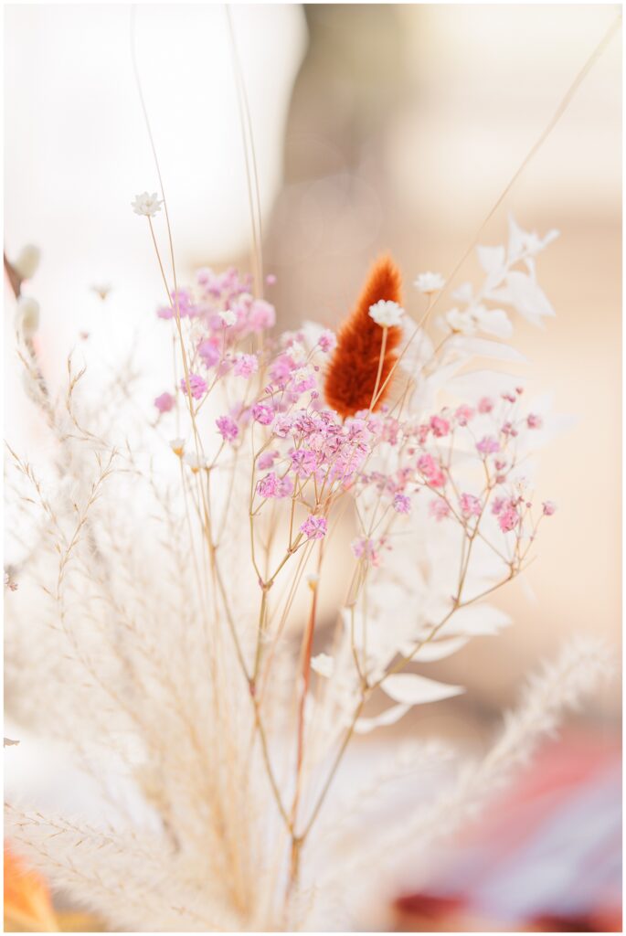 A delicate arrangement of dried flowers in pastel tones at a wedding reception, including soft pink flowers, white accents, and an orange sprig, creating a soft and romantic ambiance on the table at the Colonial Hotel in Gardner, MA.