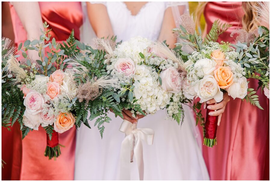 Bridesmaids at a fall wedding at the Colonial Hotel in Gardner, MA, hold bouquets featuring a mix of white and peach roses, Queen Anne’s lace, ferns, eucalyptus, and wispy pampas grass, perfectly complementing their terracotta-colored dresses.