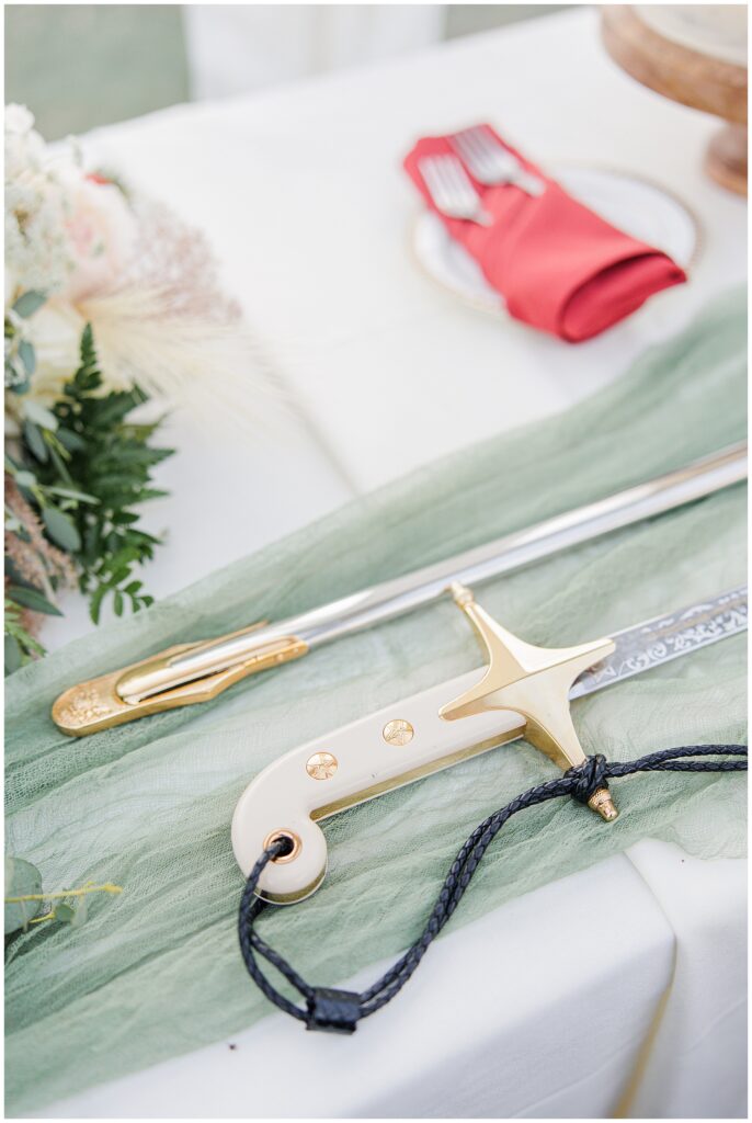 A decorative ceremonial sword with a white and gold hilt, laid on a soft green cloth on a table at the Colonial Hotel wedding, adding a unique and elegant touch to the wedding decor.