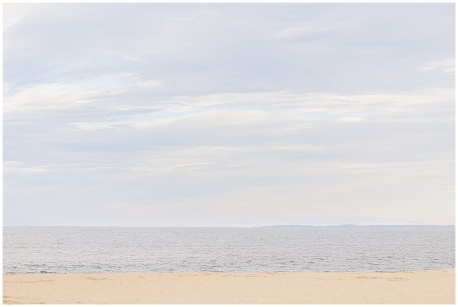 A serene view of the ocean from the sandy shore of a private beach in Newburyport, MA, with the horizon blending into the cloudy sky.