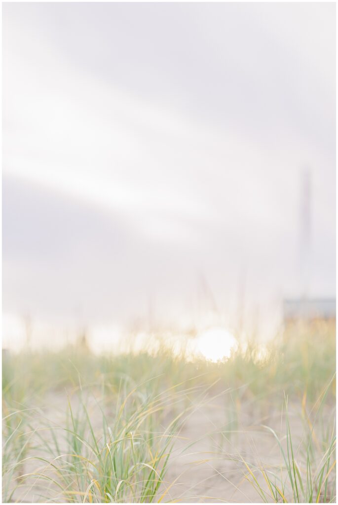 A blurred sunset scene with beach grass in the foreground, creating a soft, warm atmosphere during a senior photo session at a private beach in Newburyport, MA.