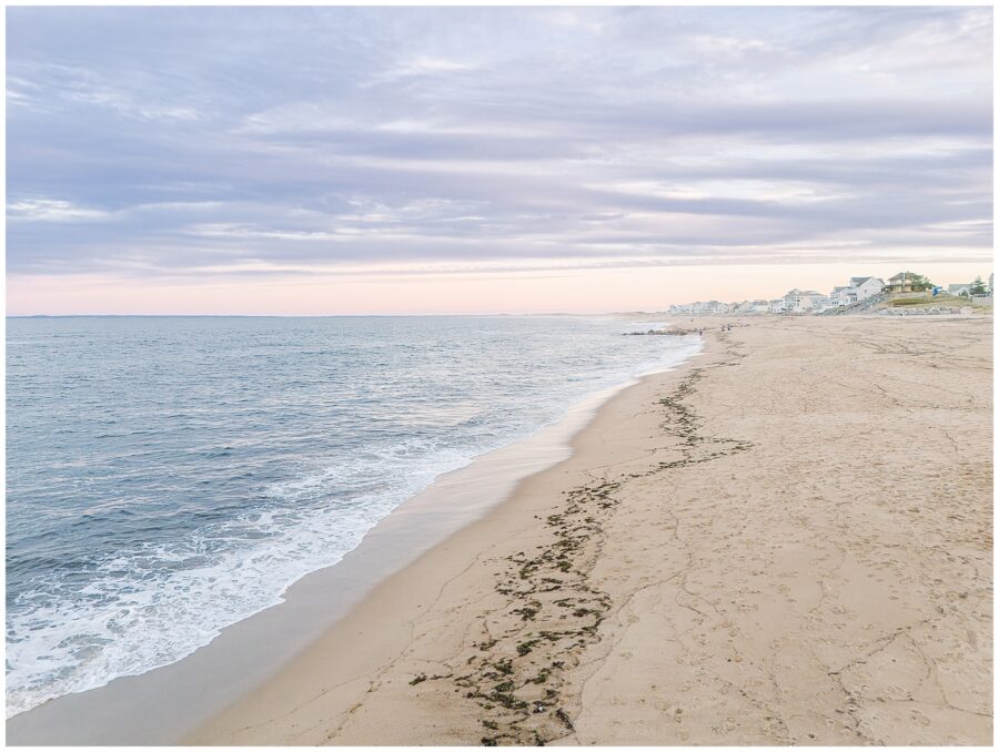 A scenic view of the private beach in Newburyport, MA, at sunset. The coastline stretches into the distance, with soft pastel skies and calm ocean waters.