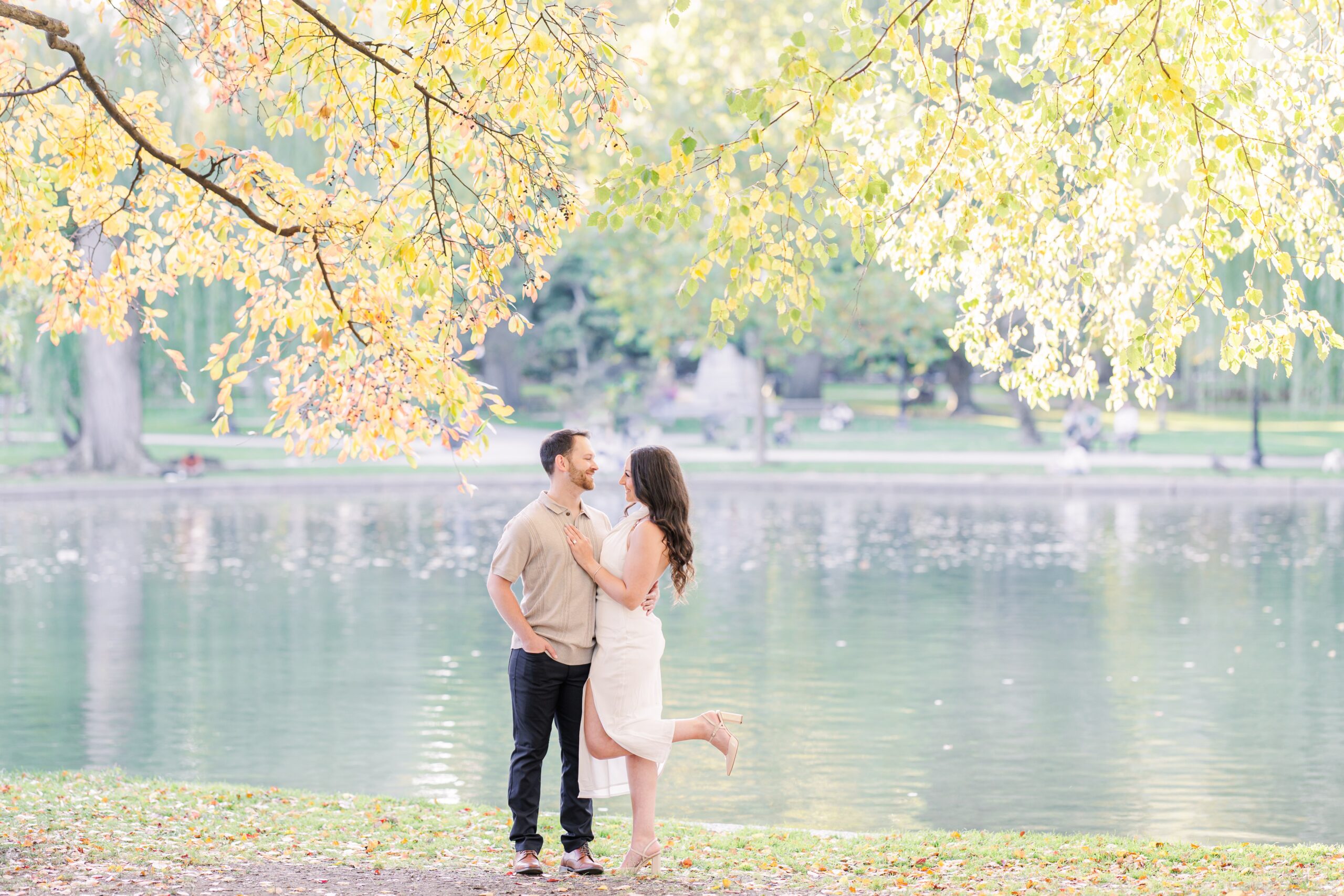 The couple stands closely, framed by bright fall foliage at Boston Public Garden. Their warm embrace against the vivid reds and oranges of the trees captures the essence of a romantic Boston engagement session.