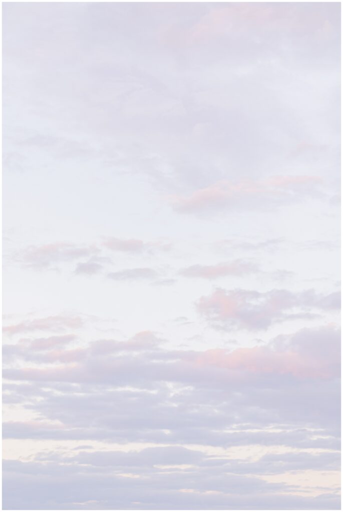 Close-up of a light, pastel-colored sky filled with soft clouds at sunset, photographed at Cohasset Beach. The colors shift from pale pinks to soft grays, creating a tranquil ambiance.