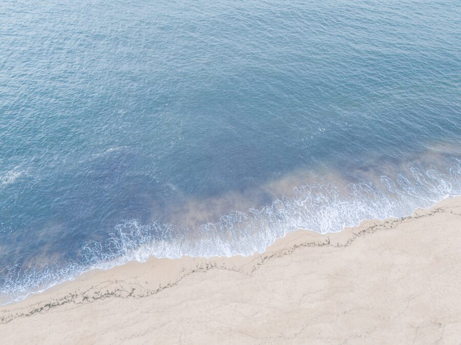 A view of gentle ocean waves meeting a sandy beach in Cape Cod. The water appears calm, with soft foam at the shoreline, creating a tranquil coastal scene.