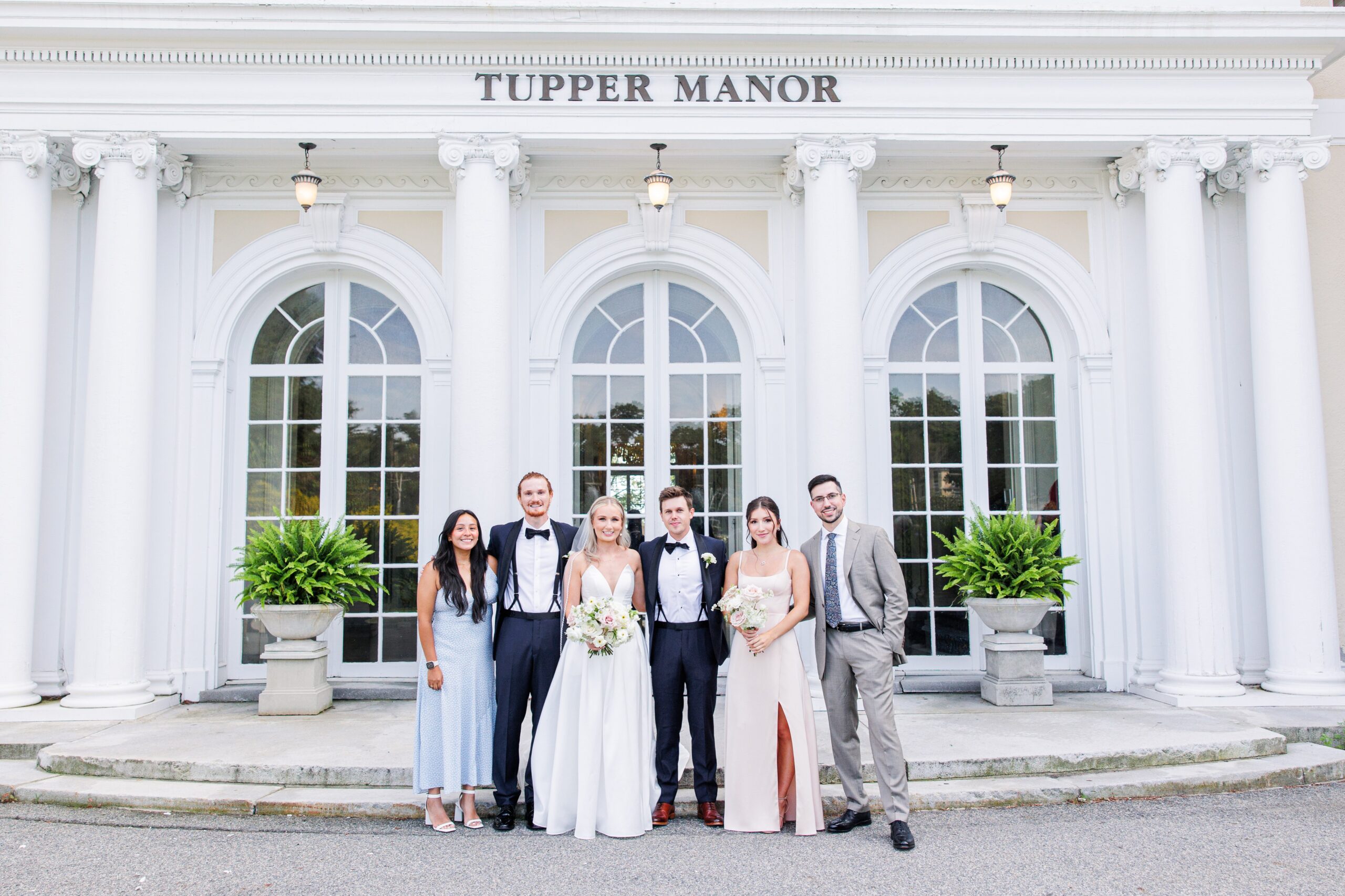Group of six people dressed in formal attire standing outside Tupper Manor, with the bride and groom centered among family and friends for classic family wedding photos.