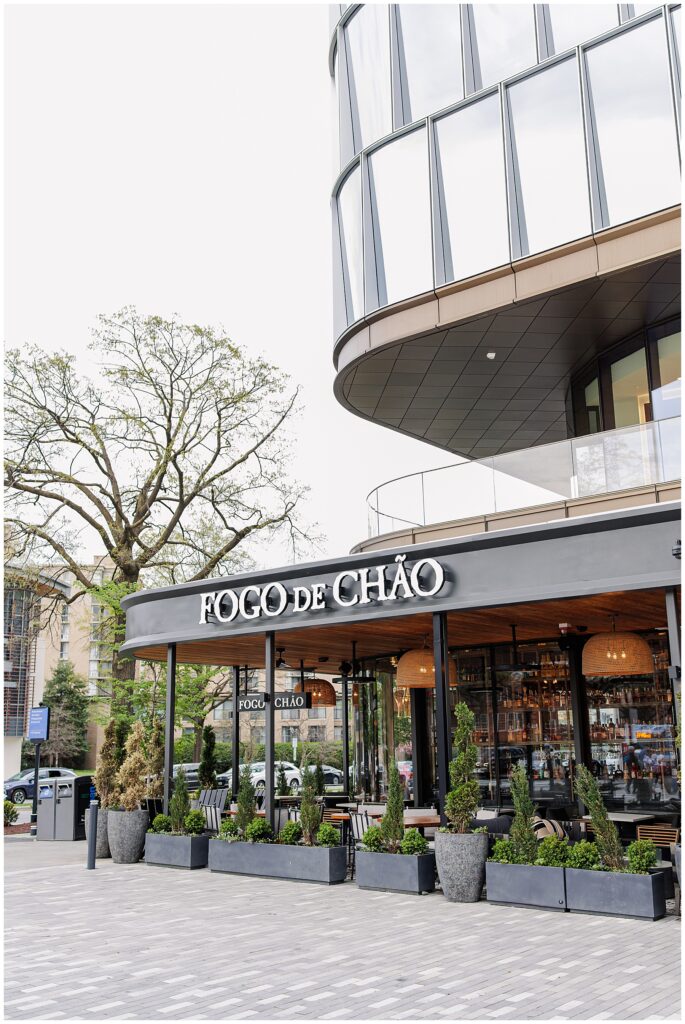 The exterior of Fogo de Chão, a Brazilian steakhouse with modern glass architecture, surrounded by potted greenery and located at The Wharf in Washington, D.C.