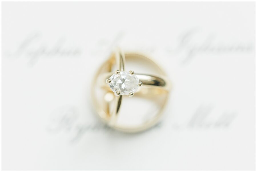 A styled flat lay of wedding invitations, ceremony programs, an engagement ring in a round box, and scattered colorful flowers on a dark fabric background, photographed by a Washington D.C. wedding photographer.