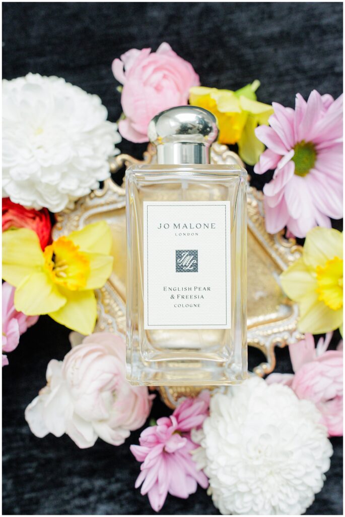 A bottle of Jo Malone English Pear & Freesia cologne surrounded by pastel flowers and gold tray details, captured by a Washington D.C. wedding photographer.