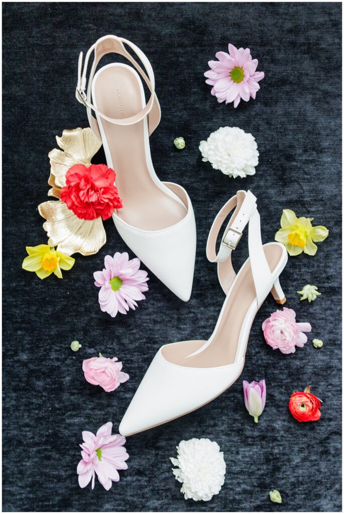 A pair of white pointed-toe heels laid out among scattered pastel flowers and gold leaf accents for a Washington D.C. wedding.