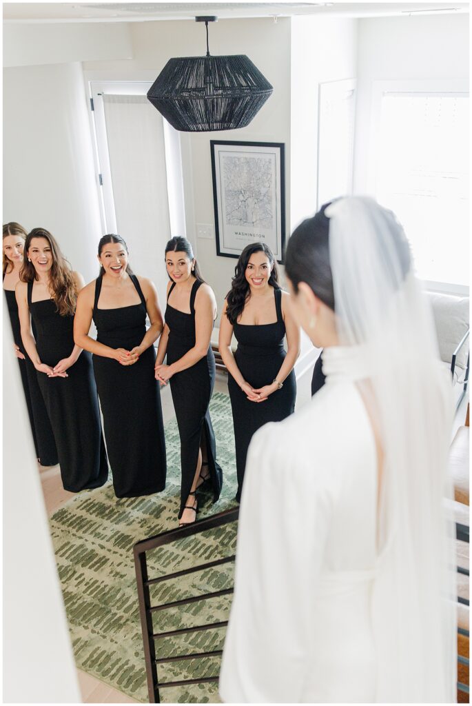 The bridesmaids burst into expressions of surprise and excitement upon seeing the bride, in a candid black-and-white photo by a Washington D.C. wedding photographer.