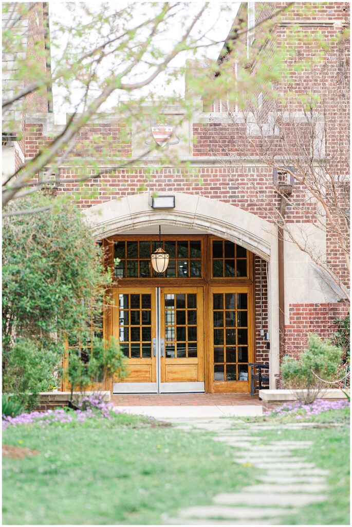 Arched wooden double doors framed by brick walls and greenery at the National Cathedral School, with a lantern-style light hanging above the entrance.