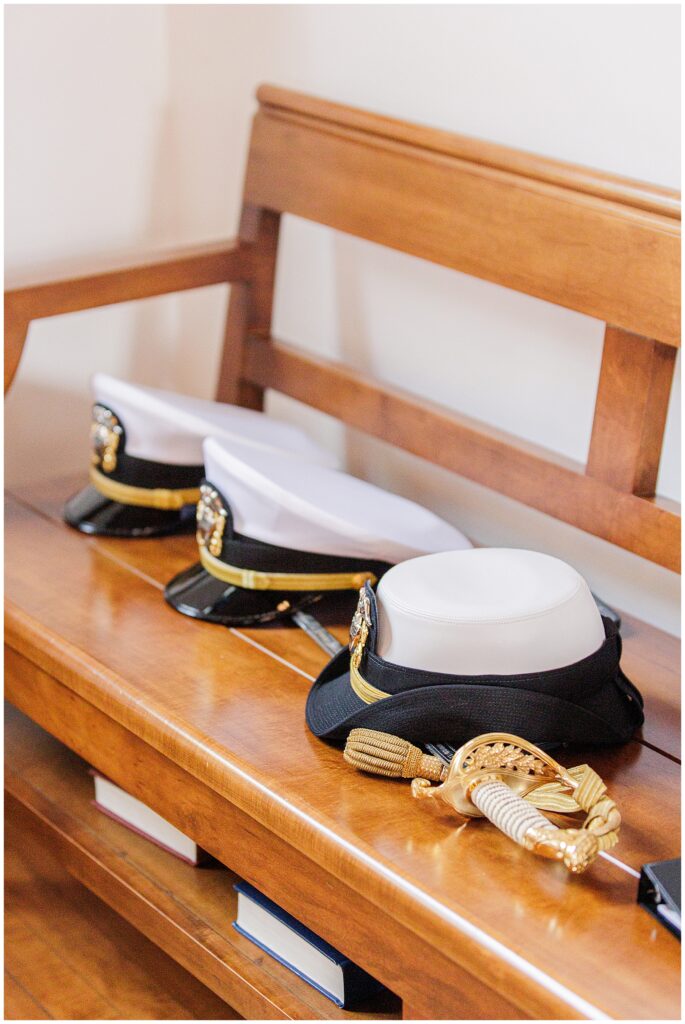 Three military dress caps and a ceremonial sword rest on a wooden pew inside the National Cathedral School chapel.