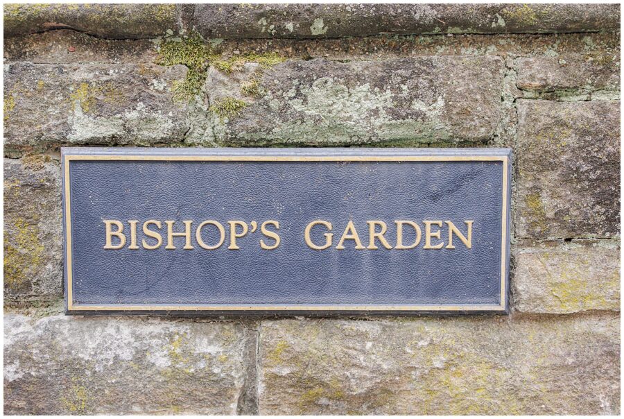 A close-up of a weathered stone wall with a plaque reading “Bishop’s Garden,” marking the location within the Washington National Cathedral grounds.
