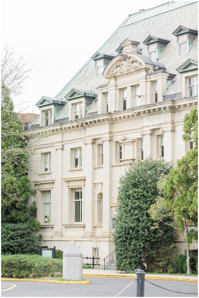 Exterior view of Hearst Hall at the National Cathedral School, showing its classic architecture with detailed stonework, tall windows, and a slate roof partially framed by trees.