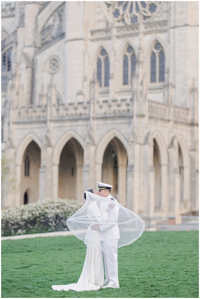 The bride and groom kiss under the bride’s flowing veil in front of the gothic architecture of the Washington National Cathedral.
