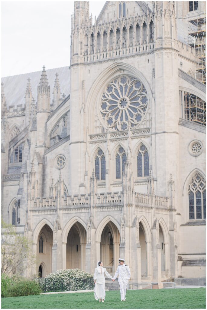 The bride and groom hold hands and walk across the lawn with the Washington National Cathedral’s intricate façade and rose window in the background.