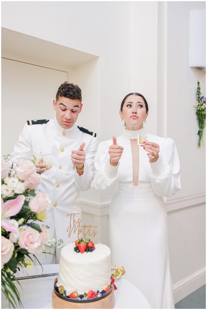 Bride and groom react with playful expressions and thumbs up while eating cake during their wedding reception at National Cathedral School.