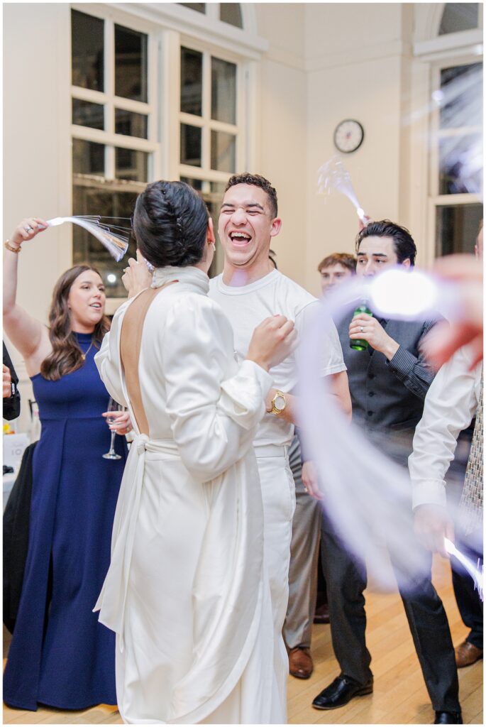 The bride and groom laugh and dance together among guests waving light-up streamers at their National Cathedral School wedding reception.