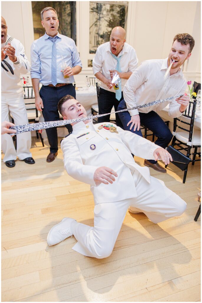 A guest in military dress uniform performs a limbo under a necktie held by others as onlookers cheer at the National Cathedral School wedding reception.