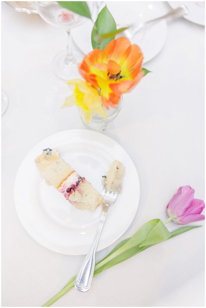 A slice of berry-filled wedding cake sits on a white plate next to a fork and a tulip on a reception table at the National Cathedral School.