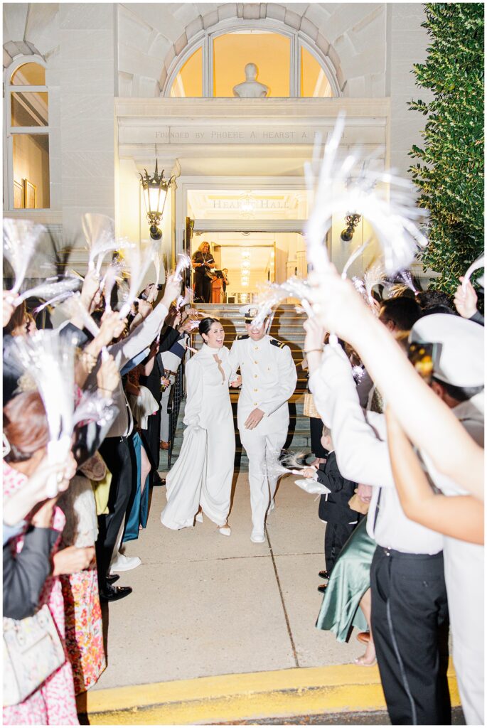 The bride and groom make their grand exit from Hearst Hall at the National Cathedral School, walking through a tunnel of guests waving light-up streamers.