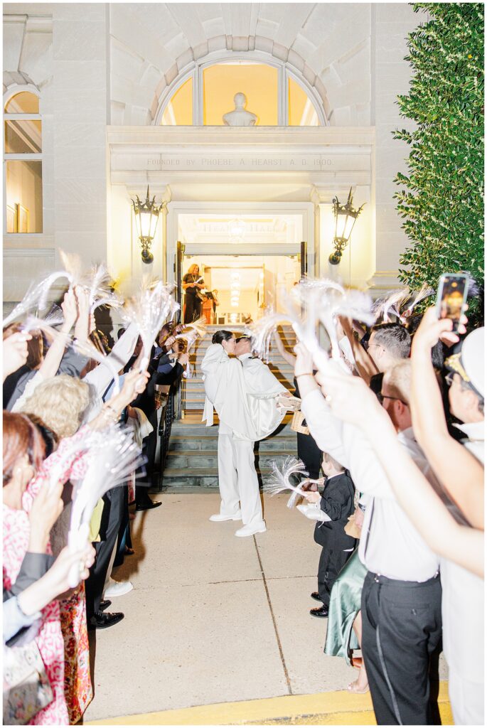 The groom lifts the bride in a kiss under a tunnel of waving streamers as they exit Hearst Hall at the National Cathedral School.