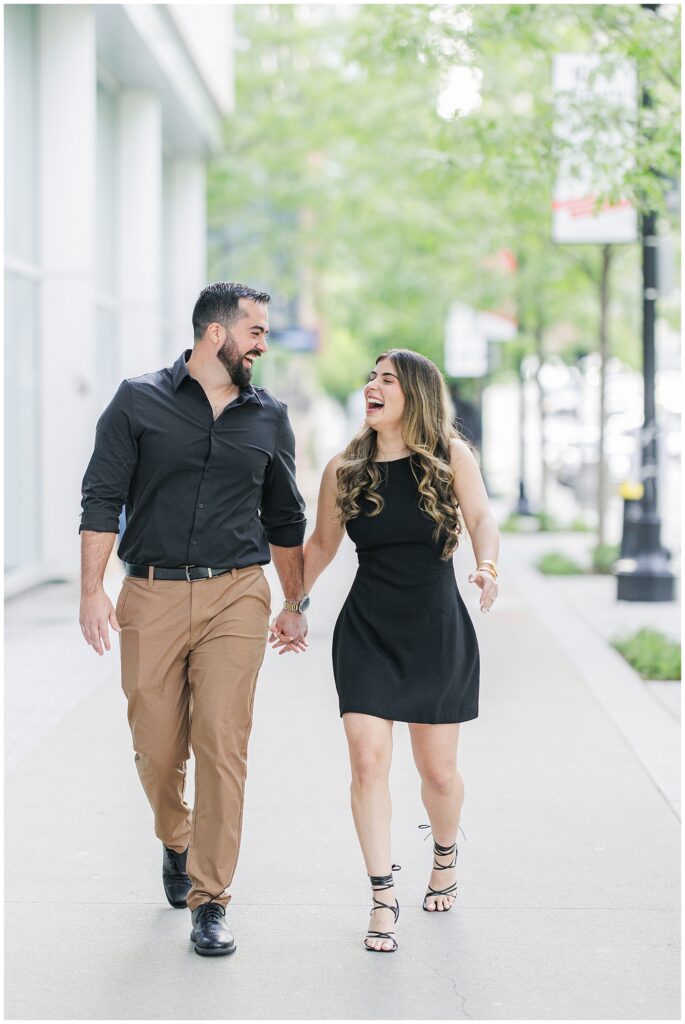 The couple walks hand-in-hand down a sidewalk in Boston’s Seaport district, smiling and laughing after their Deck 12 Boston proposal.