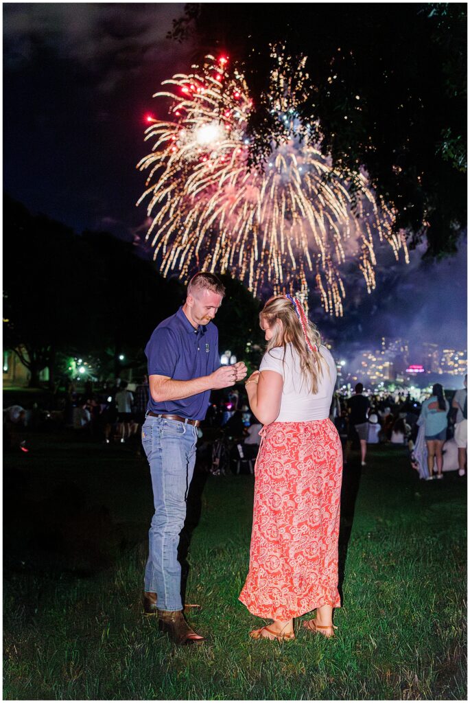 A man places a ring on his partner’s finger during a proposal under Boston’s 4th of July fireworks.