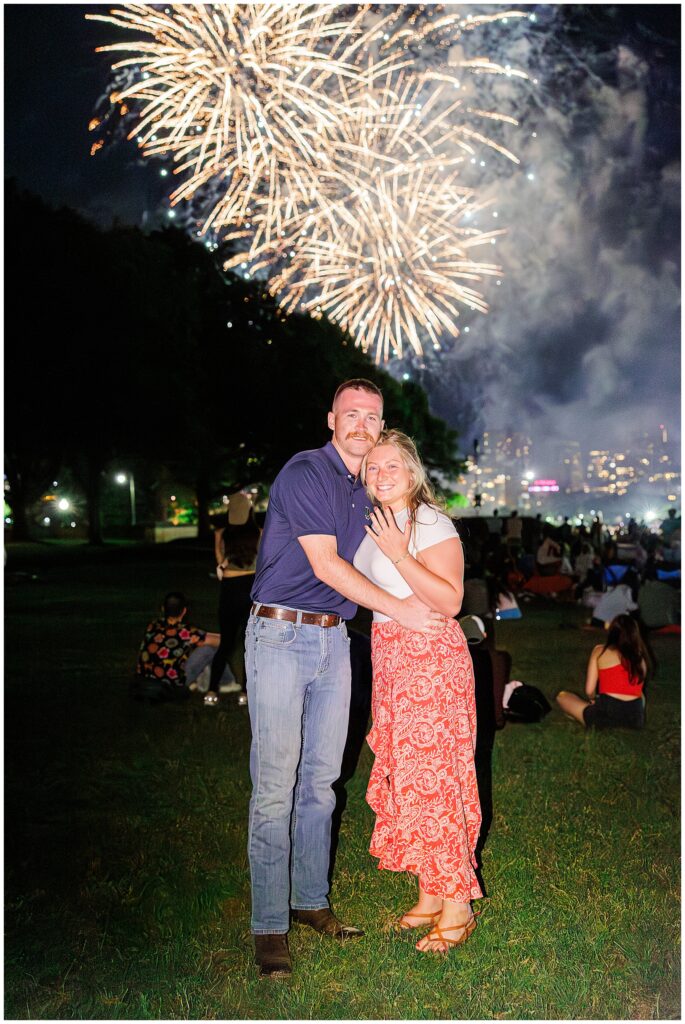 A newly engaged couple smiles for a photo under golden fireworks in Boston, celebrating a proposal moment filled with joy.