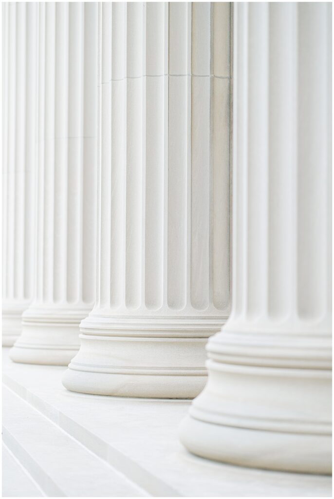 A close-up view of a row of tall, fluted stone columns with wide bases, part of MIT’s classical architecture. Captured by a Cambridge photographer.