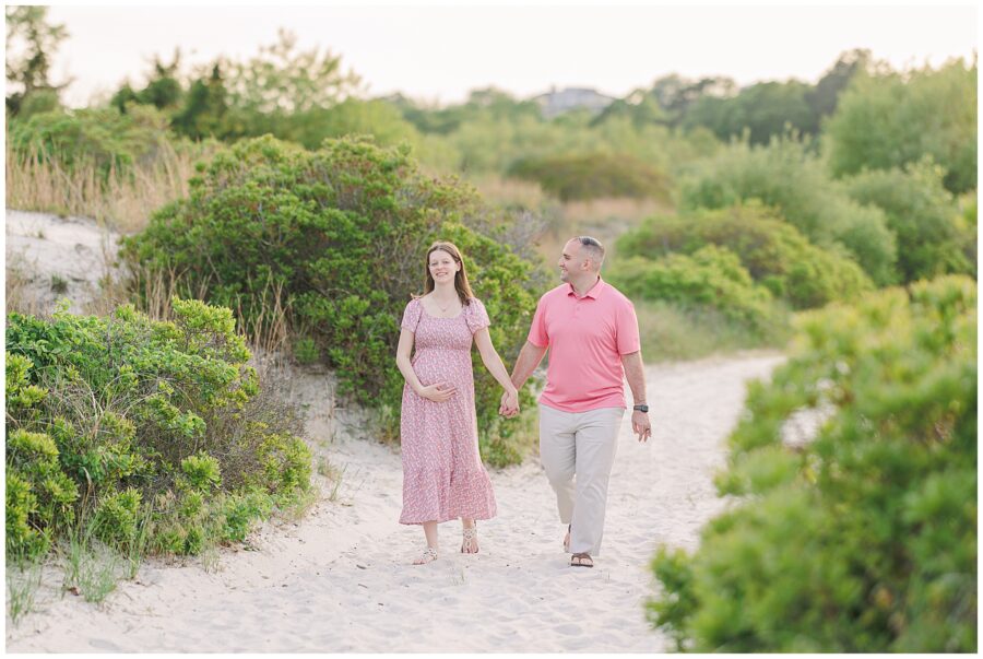A pregnant woman stands barefoot on the beach at Wingaersheek, gently holding her belly while looking down.