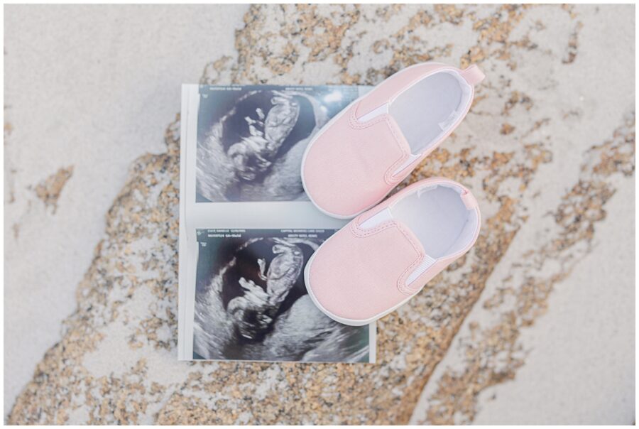  Pink baby shoes placed on ultrasound prints on a sandy rock at Wingaersheek Beach.