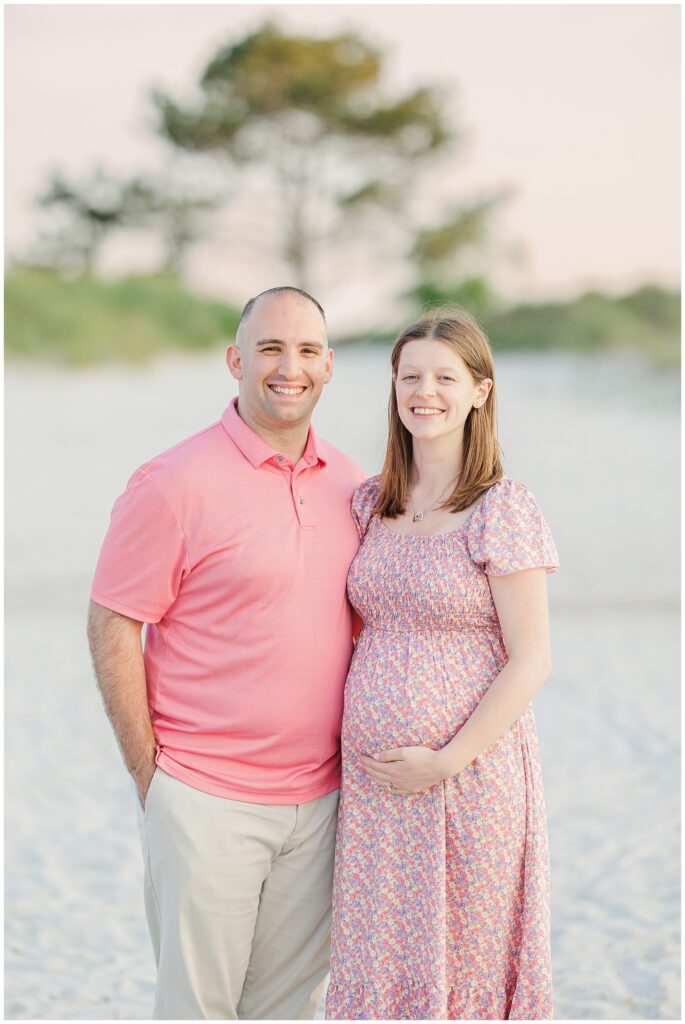 Smiling couple standing on the beach at Wingaersheek Beach during their maternity session.