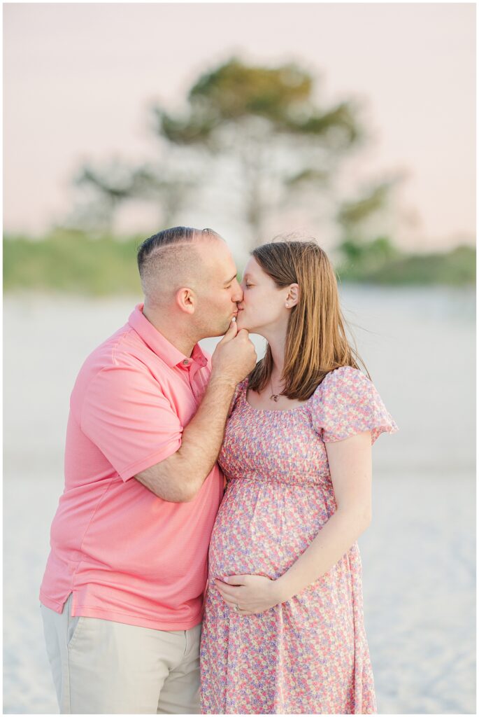 Close-up of expectant couple kissing on the beach at Wingaersheek, with soft sunset light.