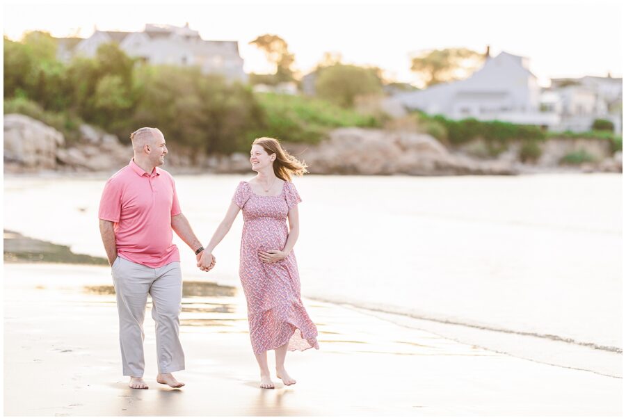 Couple walking hand in hand along the water’s edge at Wingaersheek Beach during a sunset maternity session.