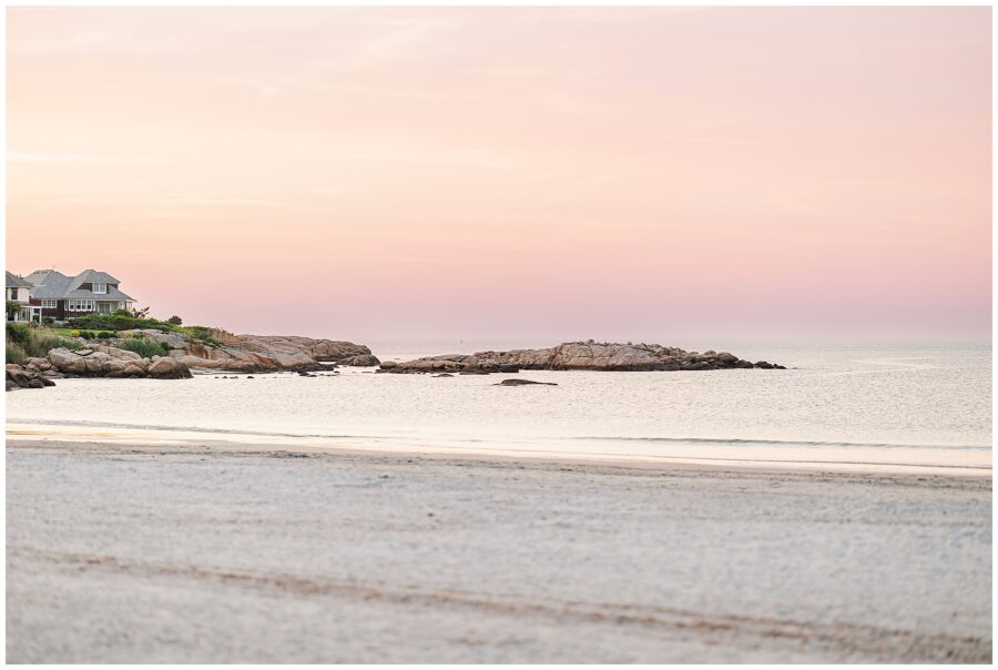 Coastal view of Wingaersheek Beach at sunset, with beach houses and pink sky over calm water.