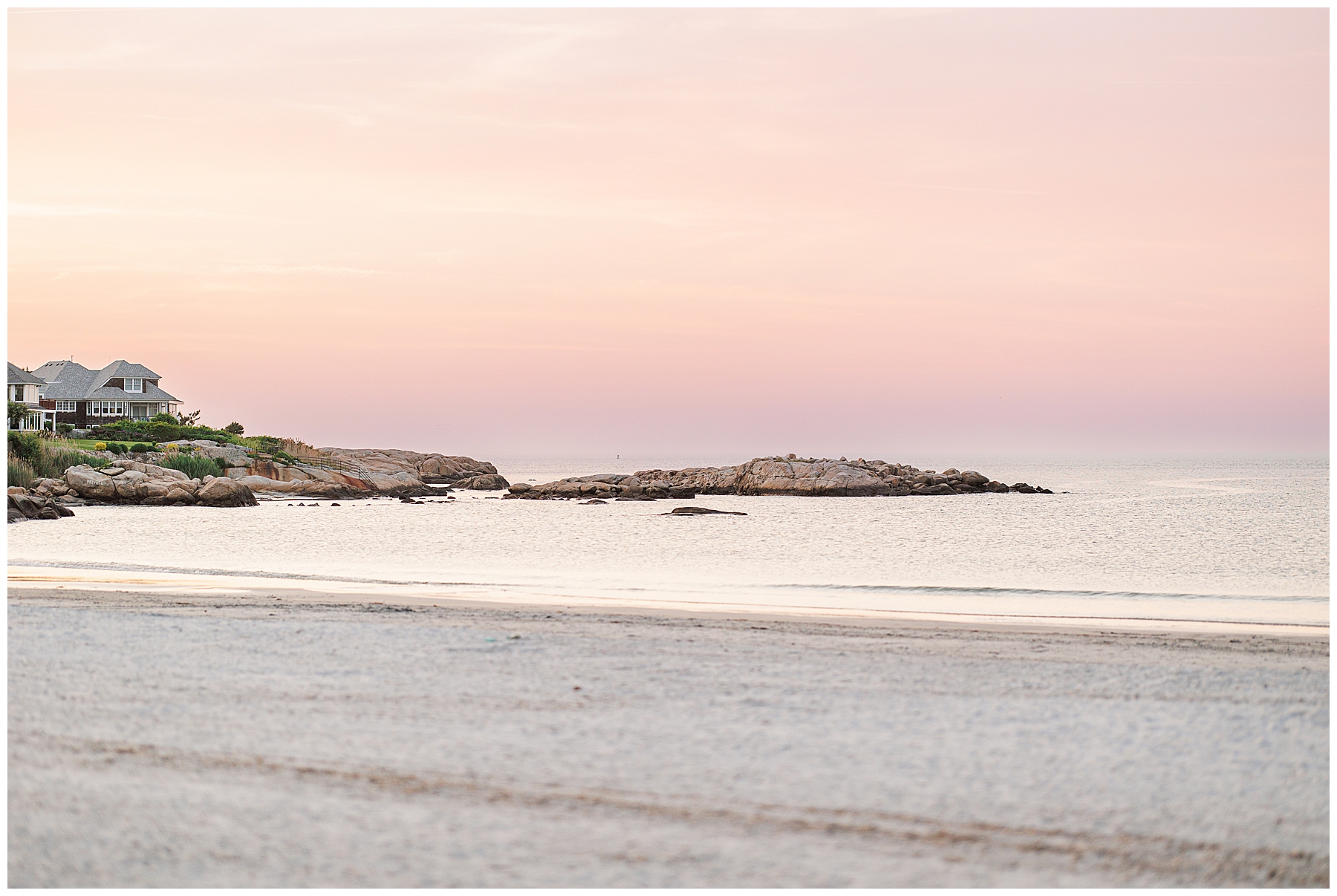 Coastal view of Wingaersheek Beach at sunset, with beach houses and pink sky over calm water.