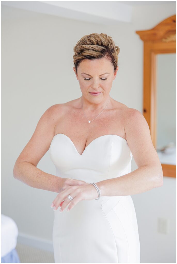 Bride in a strapless gown fastening her bracelet while getting ready in natural light. A candid wedding morning moment photographed by a Cape Cod wedding photographer.