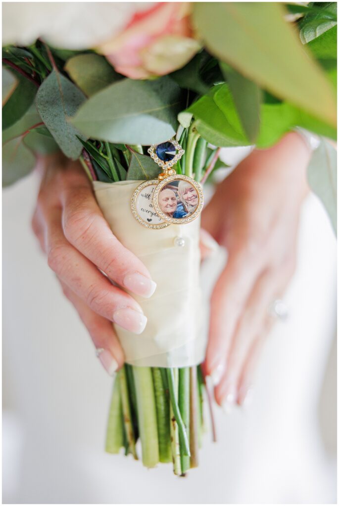 Bridal bouquet wrapped with ivory ribbon and adorned with a locket photo charm of loved ones. A sentimental wedding detail captured by a Cape Cod wedding photographer.
