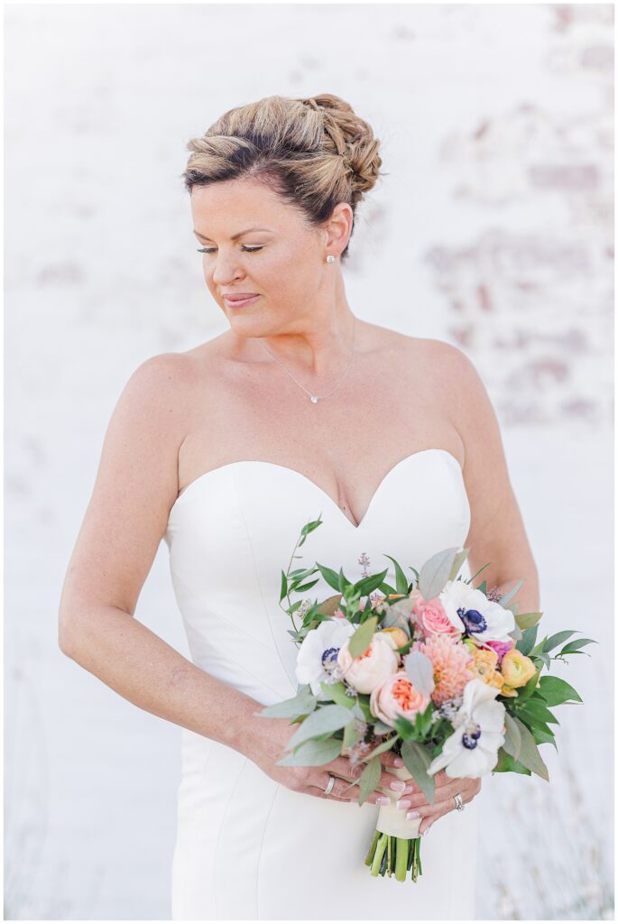 Bride in a fitted strapless gown holding her bouquet and looking down with a soft smile. A classic bridal portrait captured by a Cape Cod wedding photographer.