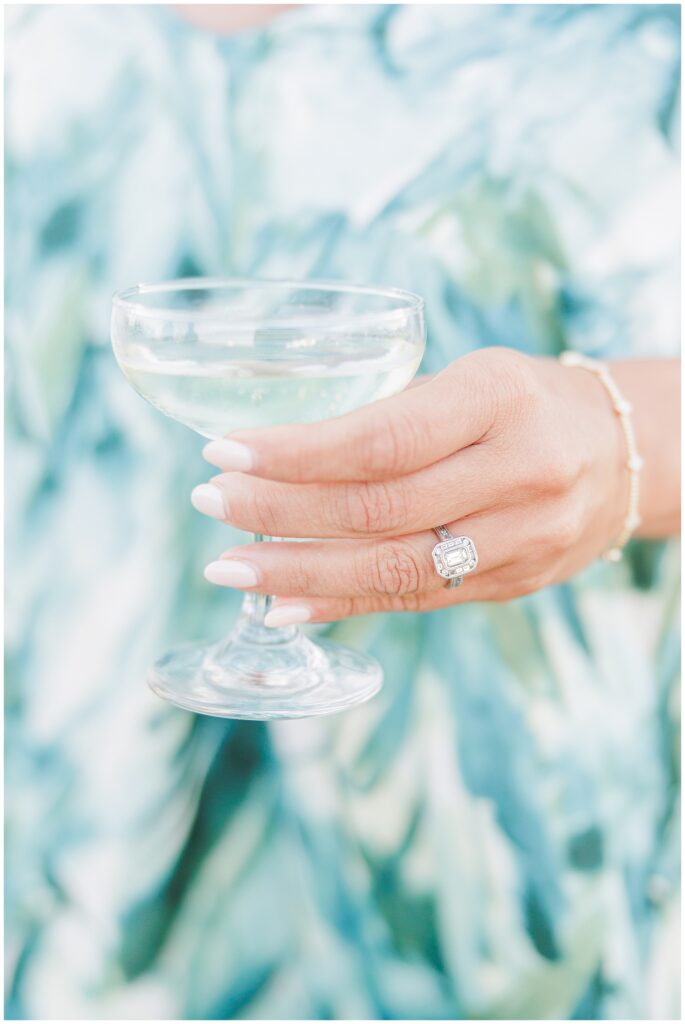 Guest holding a coupe glass of champagne with manicured nails and diamond engagement ring. A celebratory cocktail hour moment captured by a Cape Cod wedding photographer.