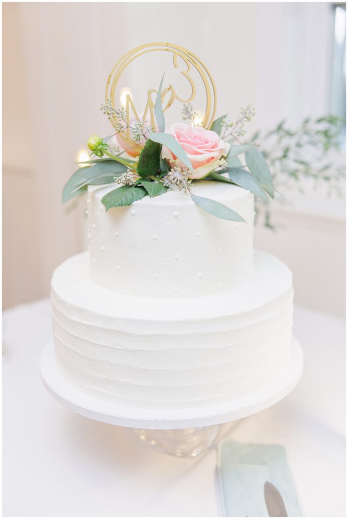 Two-tier white wedding cake decorated with blush rose, greenery, and a gold topper. A classic Cape Cod wedding cake detail captured by a Cape Cod wedding photographer.