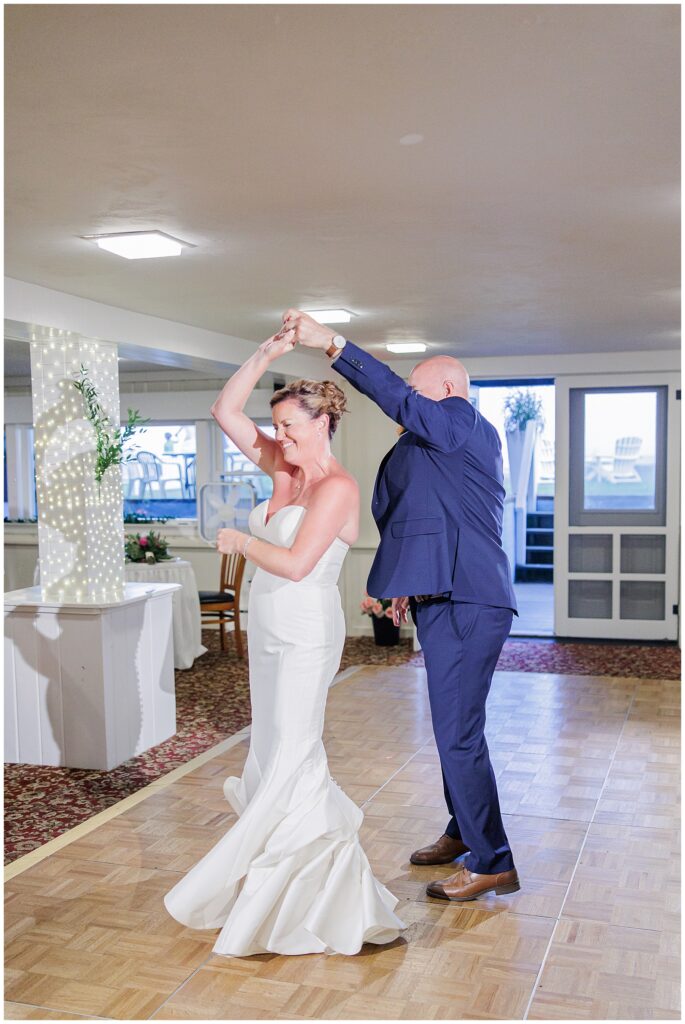 Bride and groom sharing their first dance, smiling as he twirls her on the dance floor. A joyful wedding reception moment captured by a Cape Cod wedding photographer.