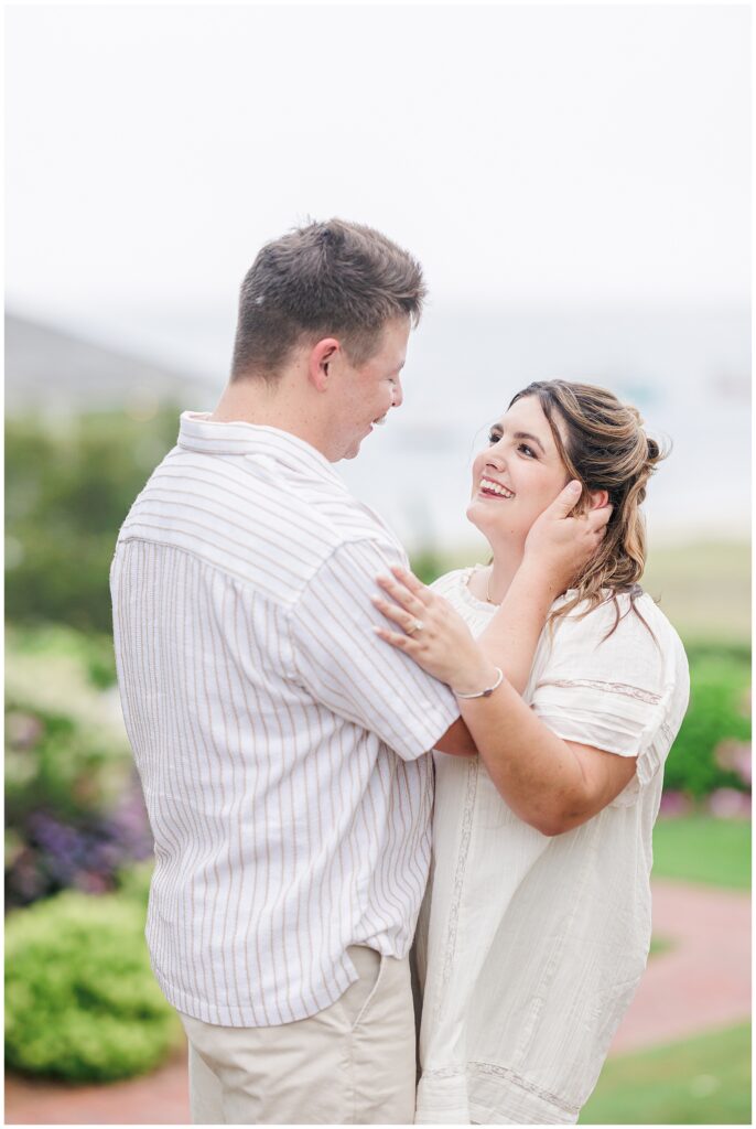 Groom-to-be holding bride-to-be’s face, smiling with Cape Cod coastline blurred in the background at Chatham Bars Inn
