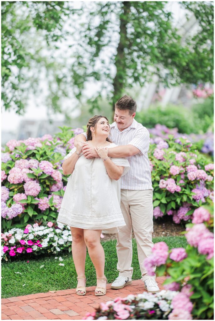 Couple laughing together in front of lush pink hydrangeas during Chatham Bars Inn engagement session