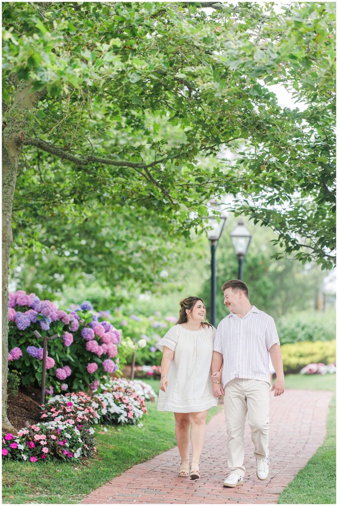 Couple walking hand in hand along hydrangea-lined brick path at Chatham Bars Inn during engagement photos