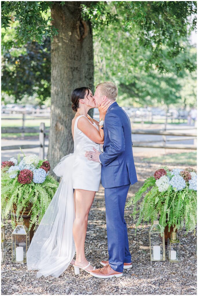 Bride and groom sharing their first kiss under a large tree during their Boston elopement ceremony.