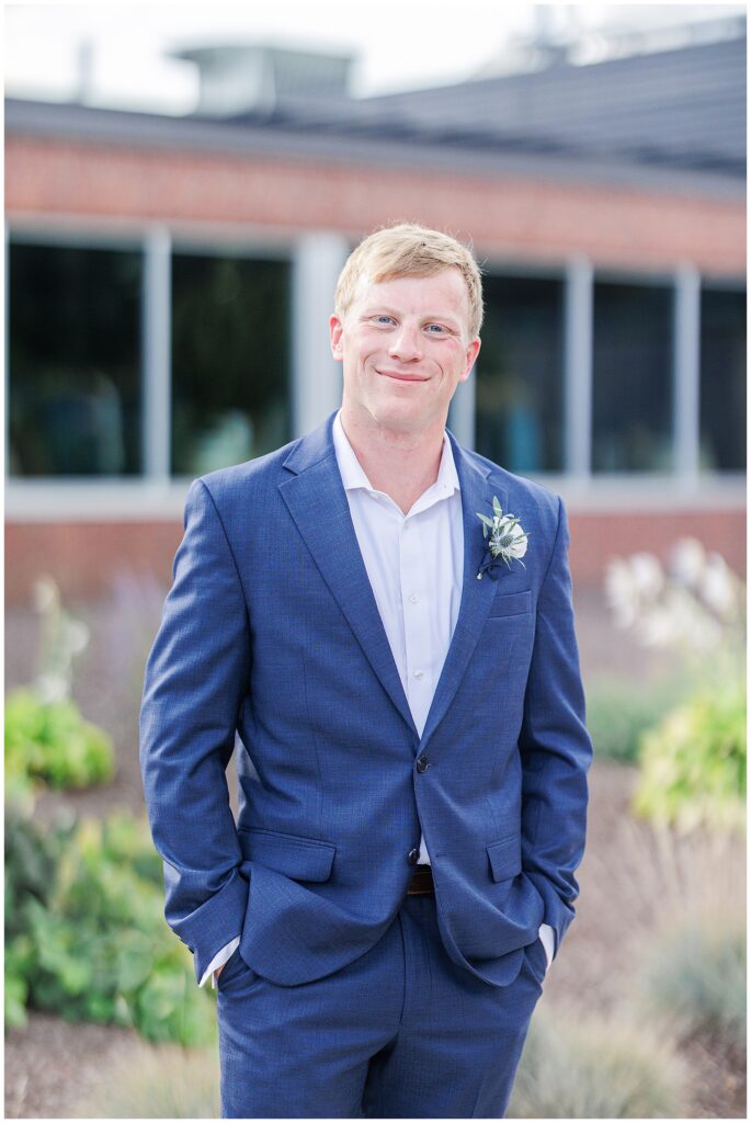 Groom in a blue suit smiling with hands in pockets, photographed by a Boston Elopement Photographer.